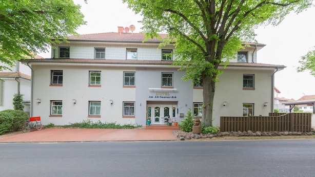 Il s’agit d’un hôtel à deux étages, sur lequel on peut lire l’inscription « HÔTEL Am Alt-Gaarder-Bek ». Il est doté d’une allée en briques rouges, d’une clôture en bois et d’un grand arbre à l’avant.