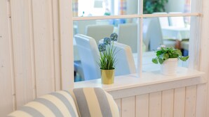 Une fenêtre donnant sur une pièce où l’on aperçoit un canapé à rayures, une petite table avec un pot de plante et un banc de fenêtre.