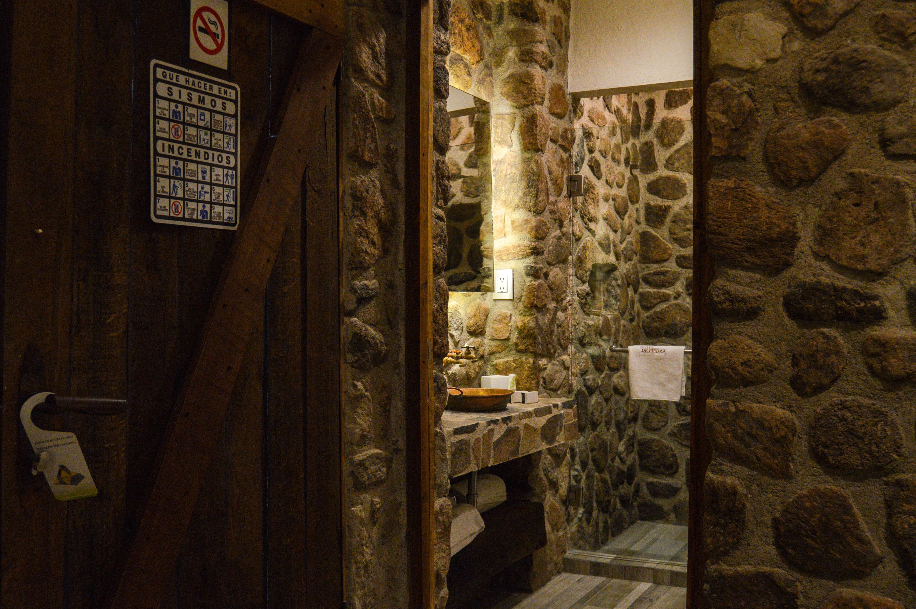 Une salle de bain aux murs de pierre, avec une serviette suspendue à un porte-serviettes, un lavabo et un panneau indiquant qu'il est interdit de fumer.