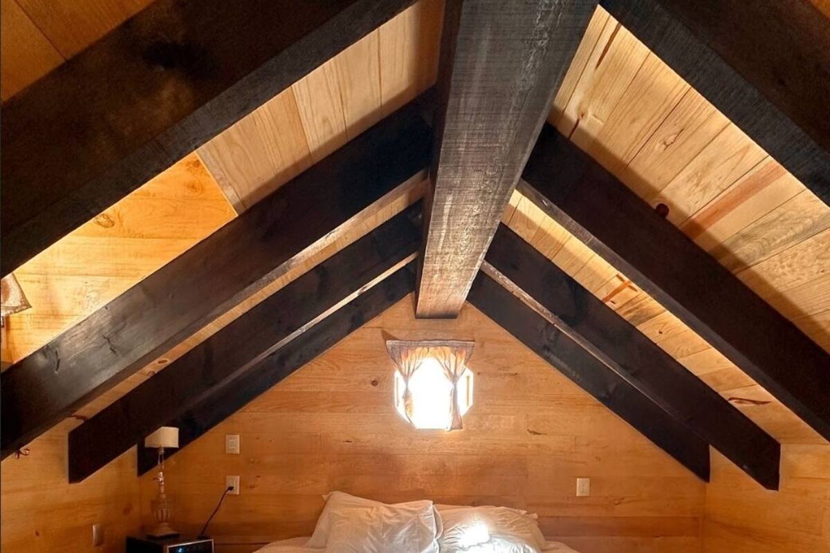 A cozy attic bedroom with a large bed, wooden beams, and a hanging light fixture.