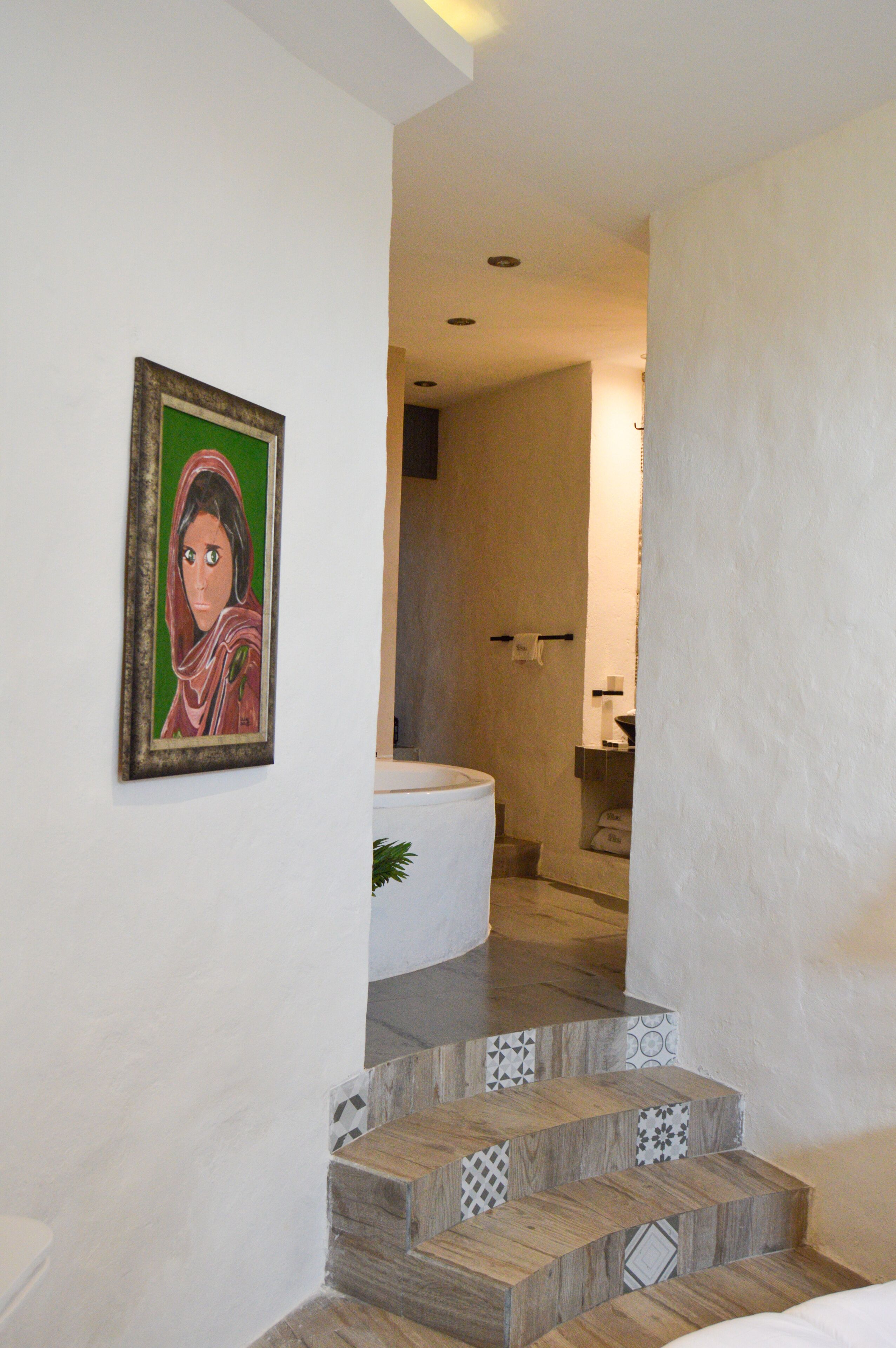 Una escalera con escalones de madera y baldosas estampadas, que conduce a un baño con bañera e inodoro.