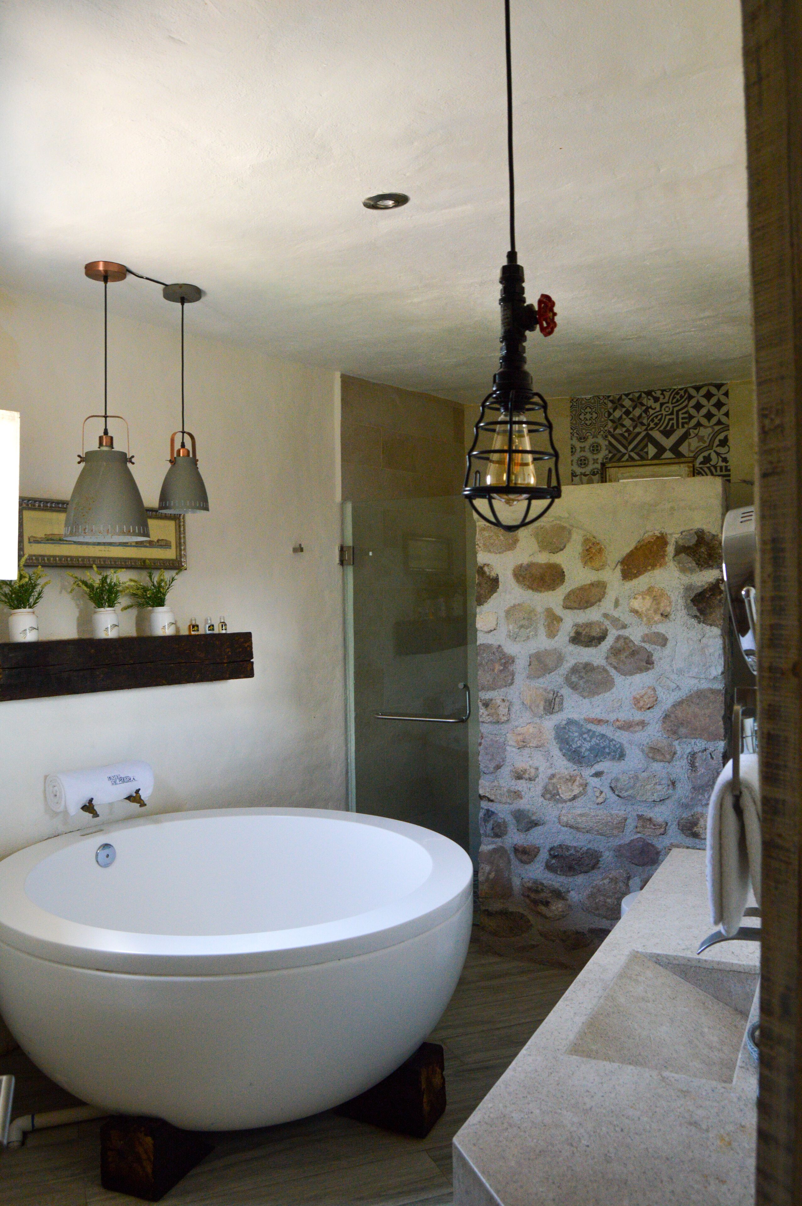 Un baño con una bañera grande, una pared de piedra y una lámpara colgante.