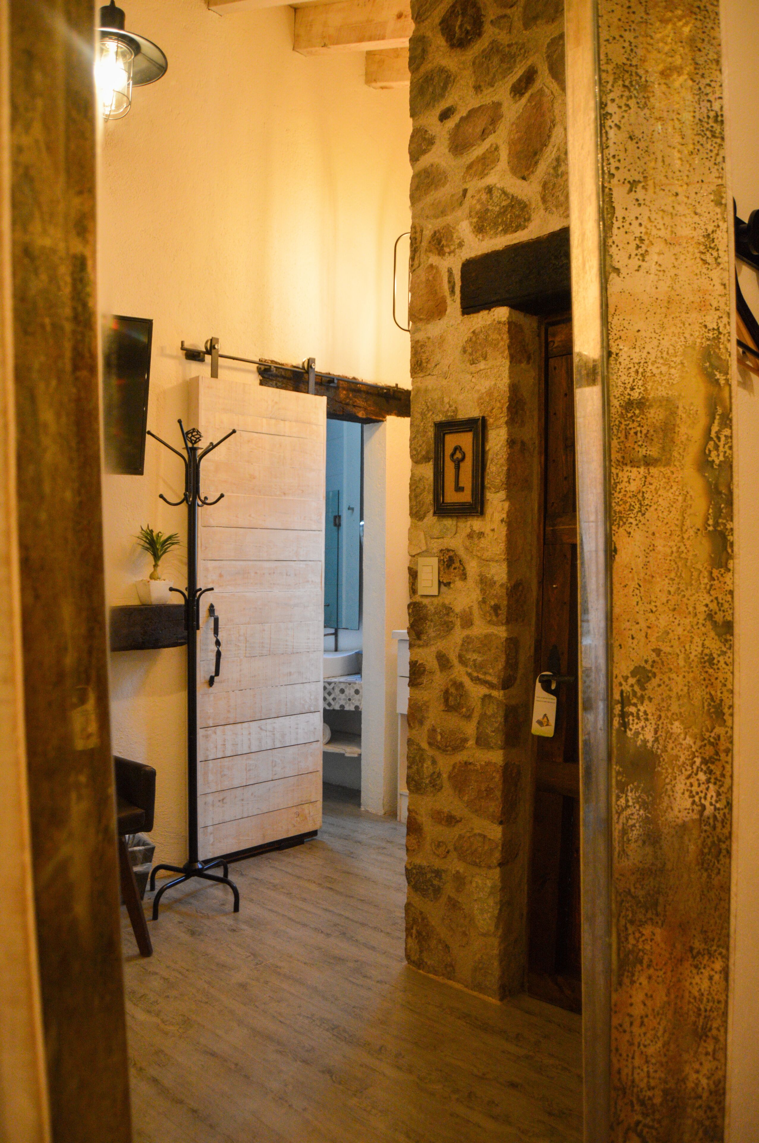 A narrow hallway with stone walls, a coat rack, a potted plant, and a door with a keyhole.
