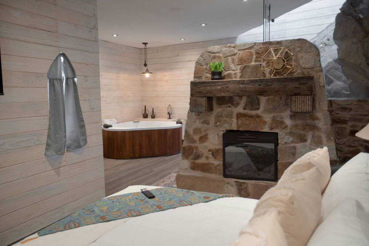 A modern bathroom with a stone fireplace, a bathtub, and a shower area.