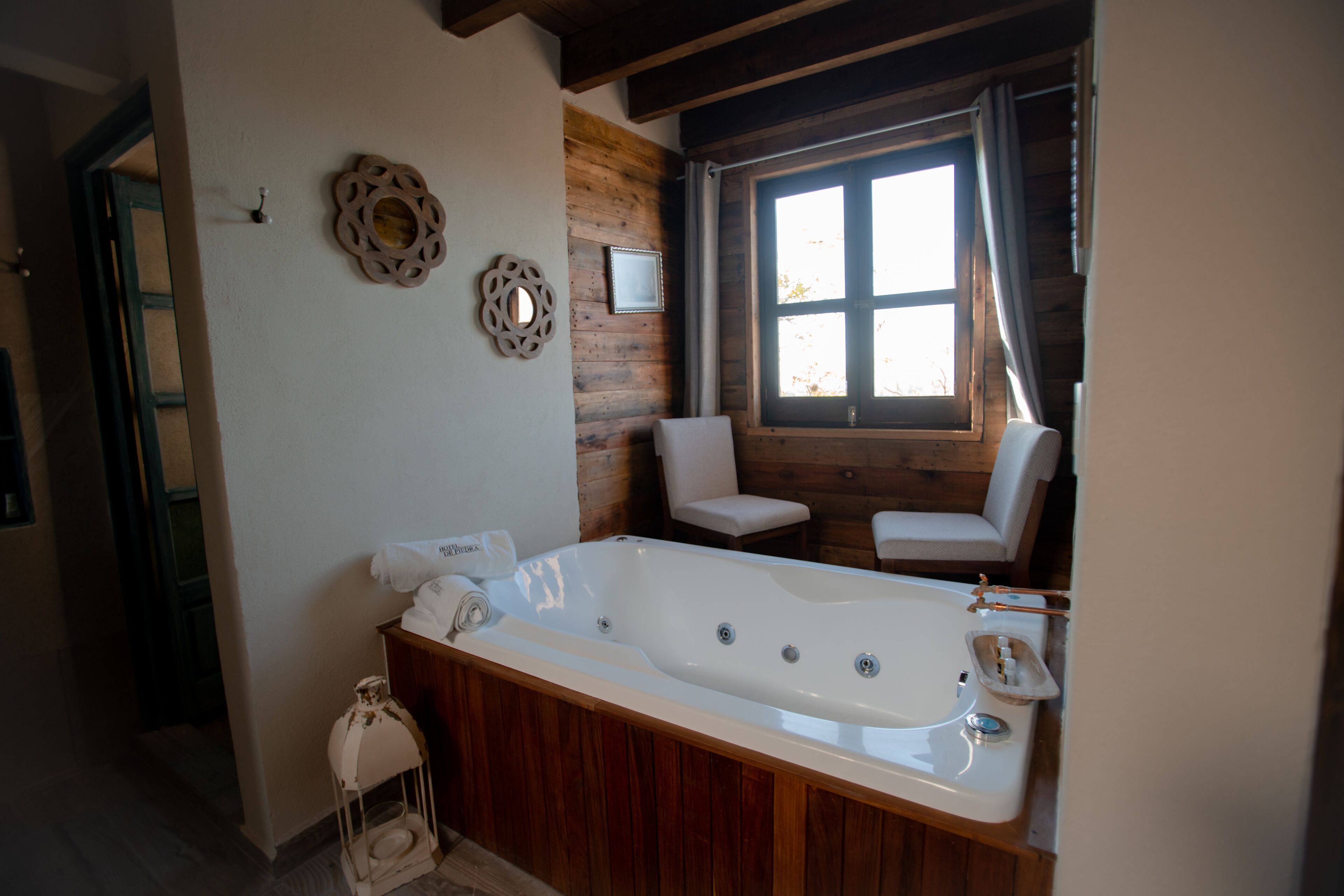 Un baño con una bañera grande, paredes de madera y una ventana con cortinas.
