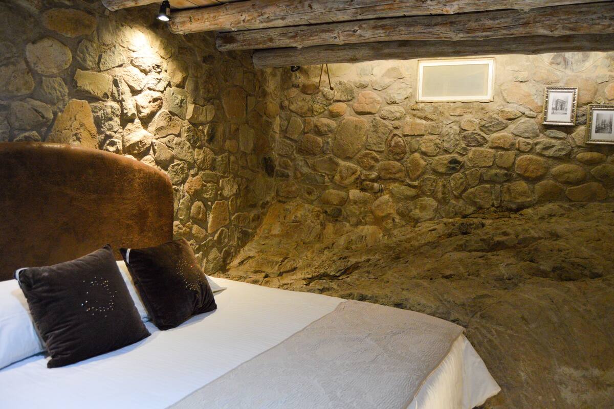 A stone-walled room with a bed, pillows, and framed pictures on the wall.