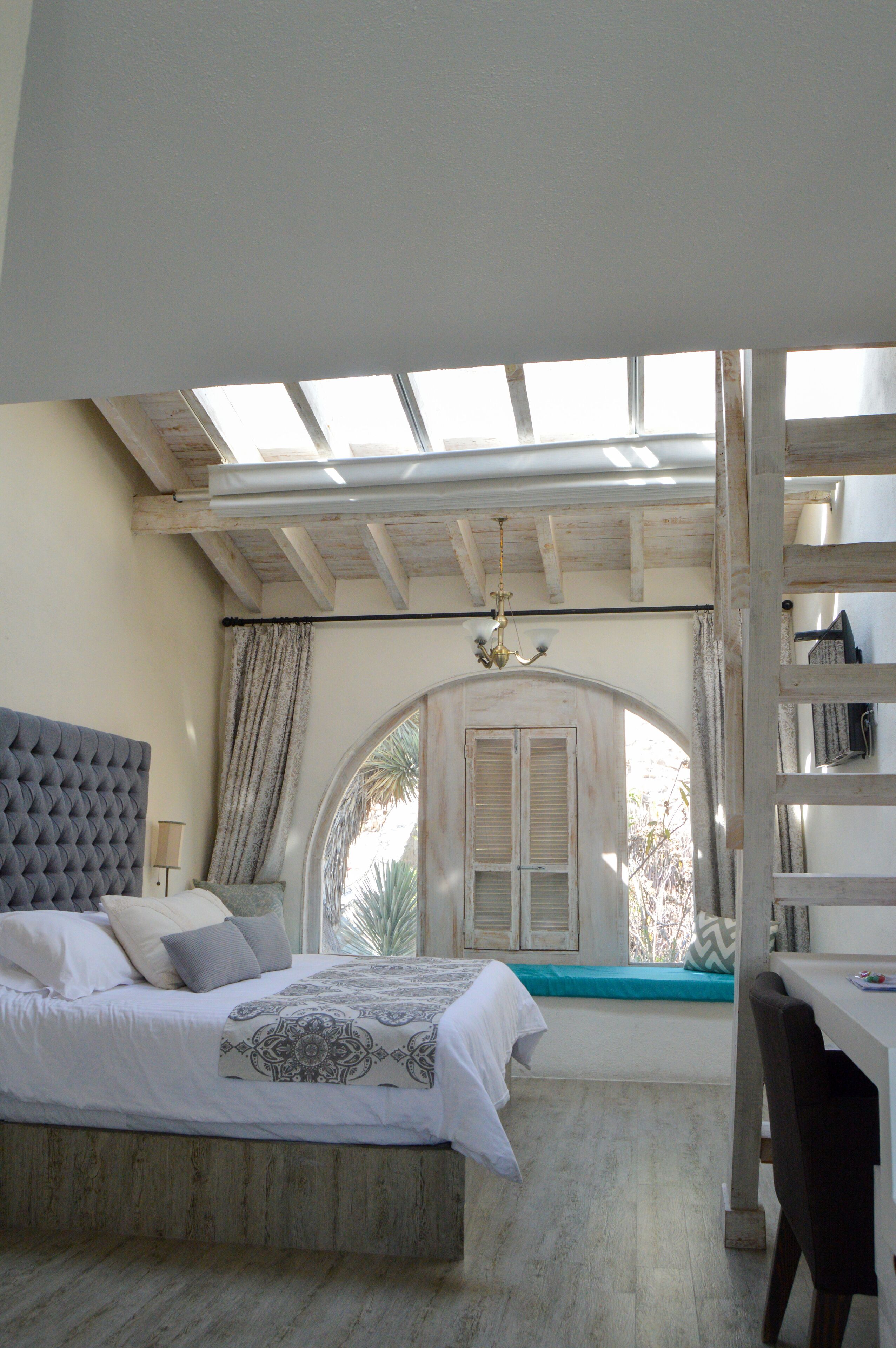 A bedroom with a bed, a desk, and a window with a view of palm trees.