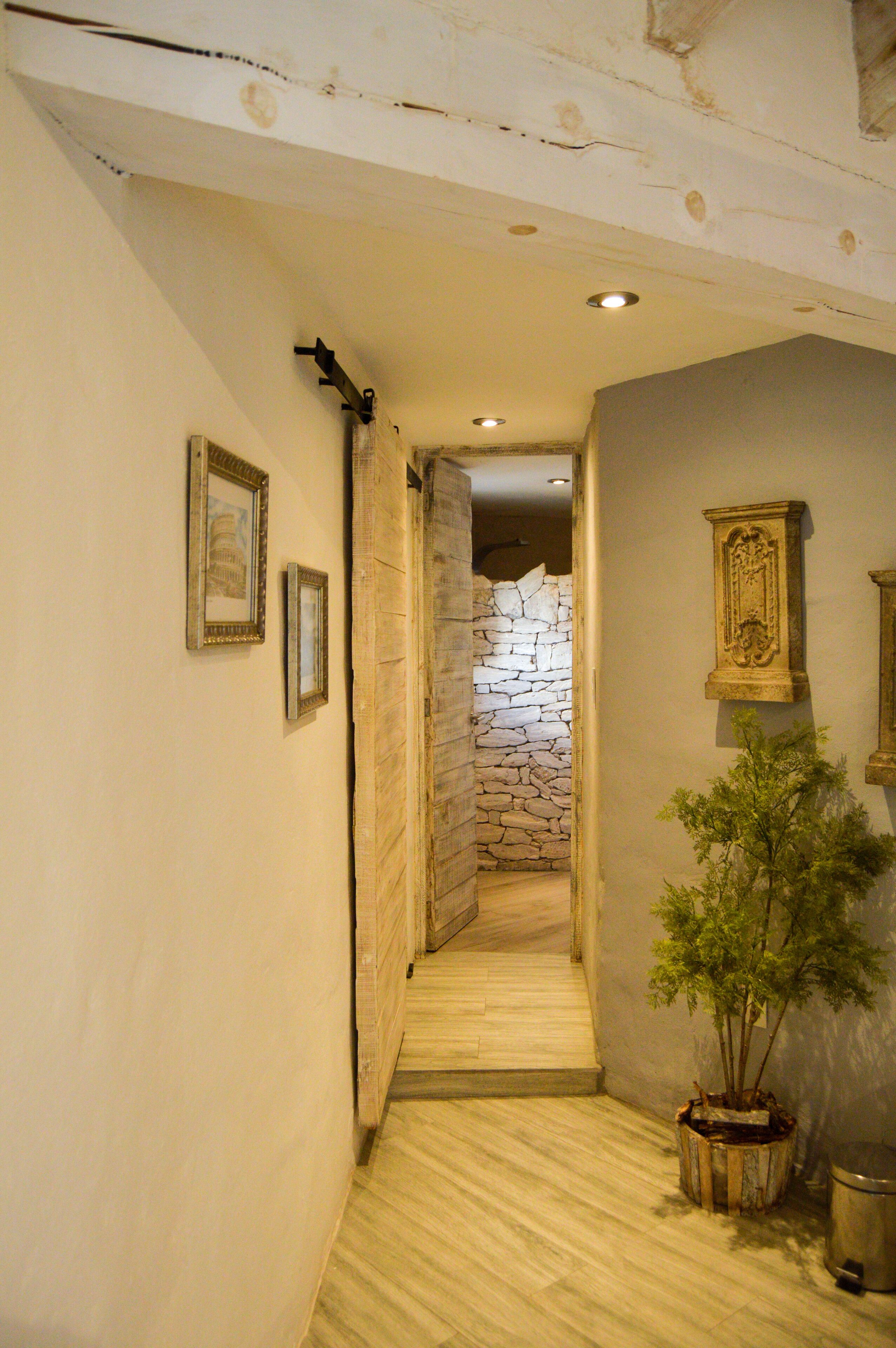 Un pasillo con pared de piedra, suelo de madera y cuadros enmarcados en las paredes.