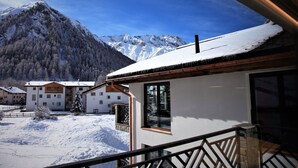 Un paysage montagneux enneigé, avec un bâtiment doté de grandes fenêtres et d’un balcon.