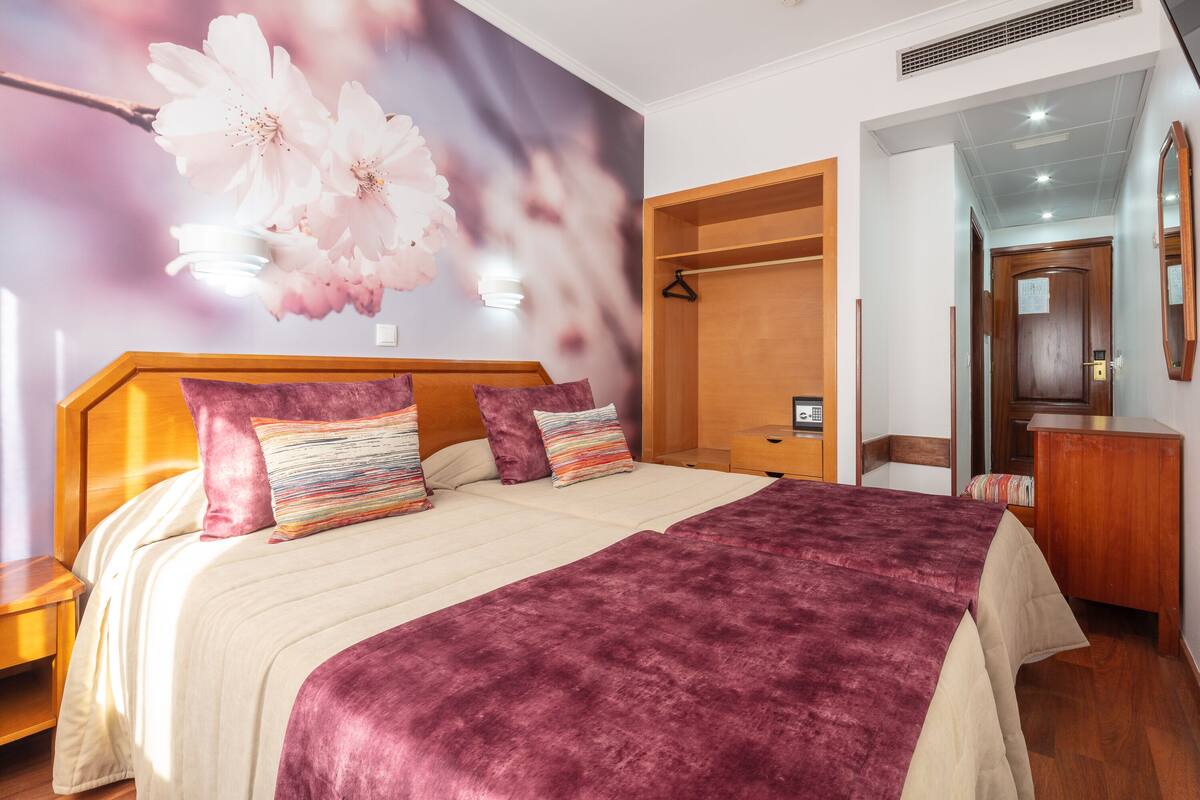 A bedroom with a large bed, a wooden wardrobe, and a mirror on the wall.