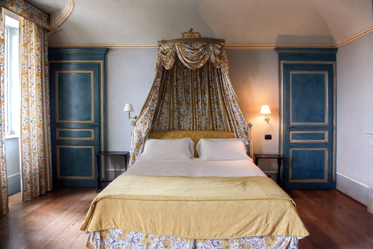 A bedroom with a four-poster bed, a canopy, and a nightstand with a lamp.