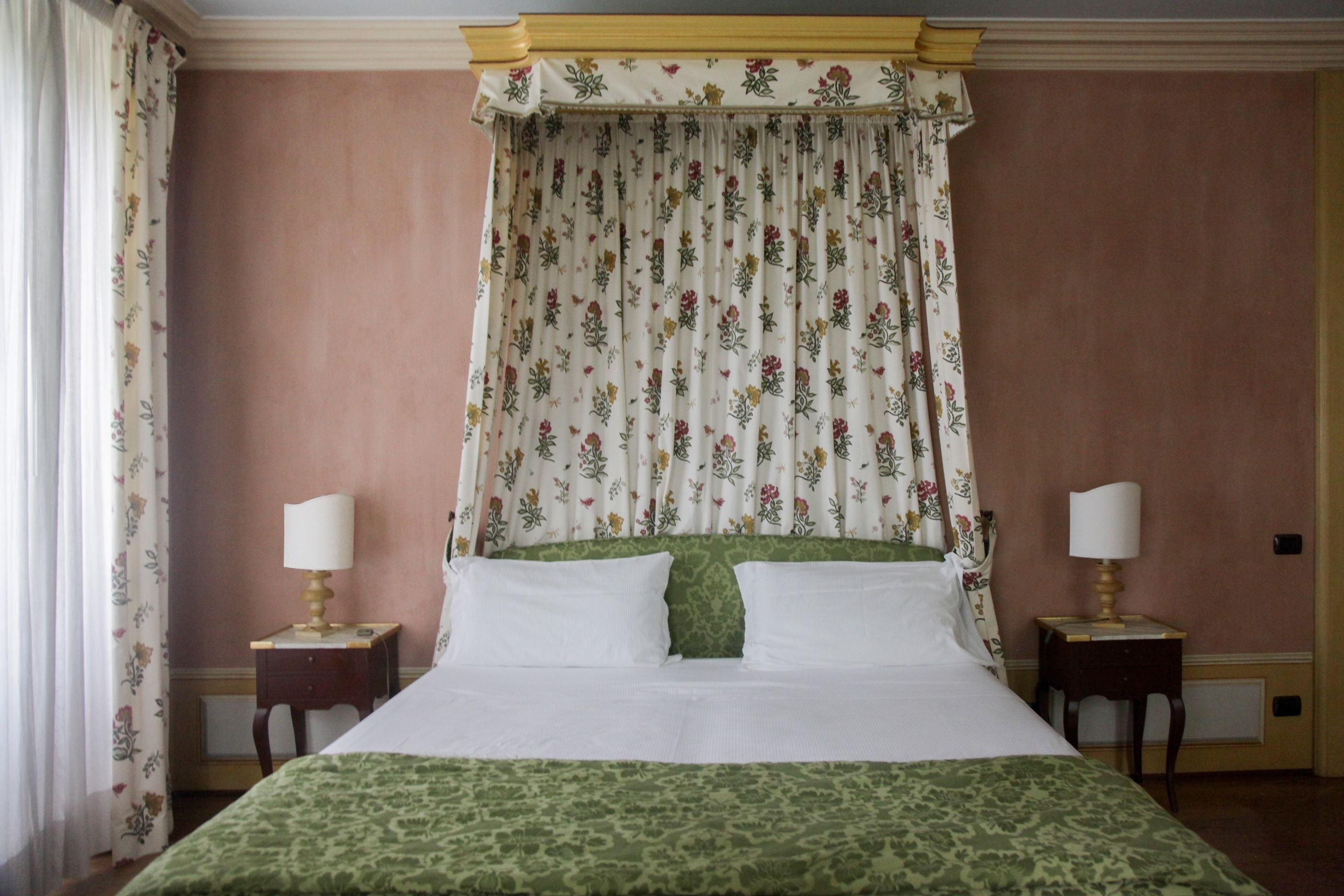 Ein Schlafzimmer mit einem Himmelbett, floralen Vorhängen und zwei Nachttischen mit Lampen.
