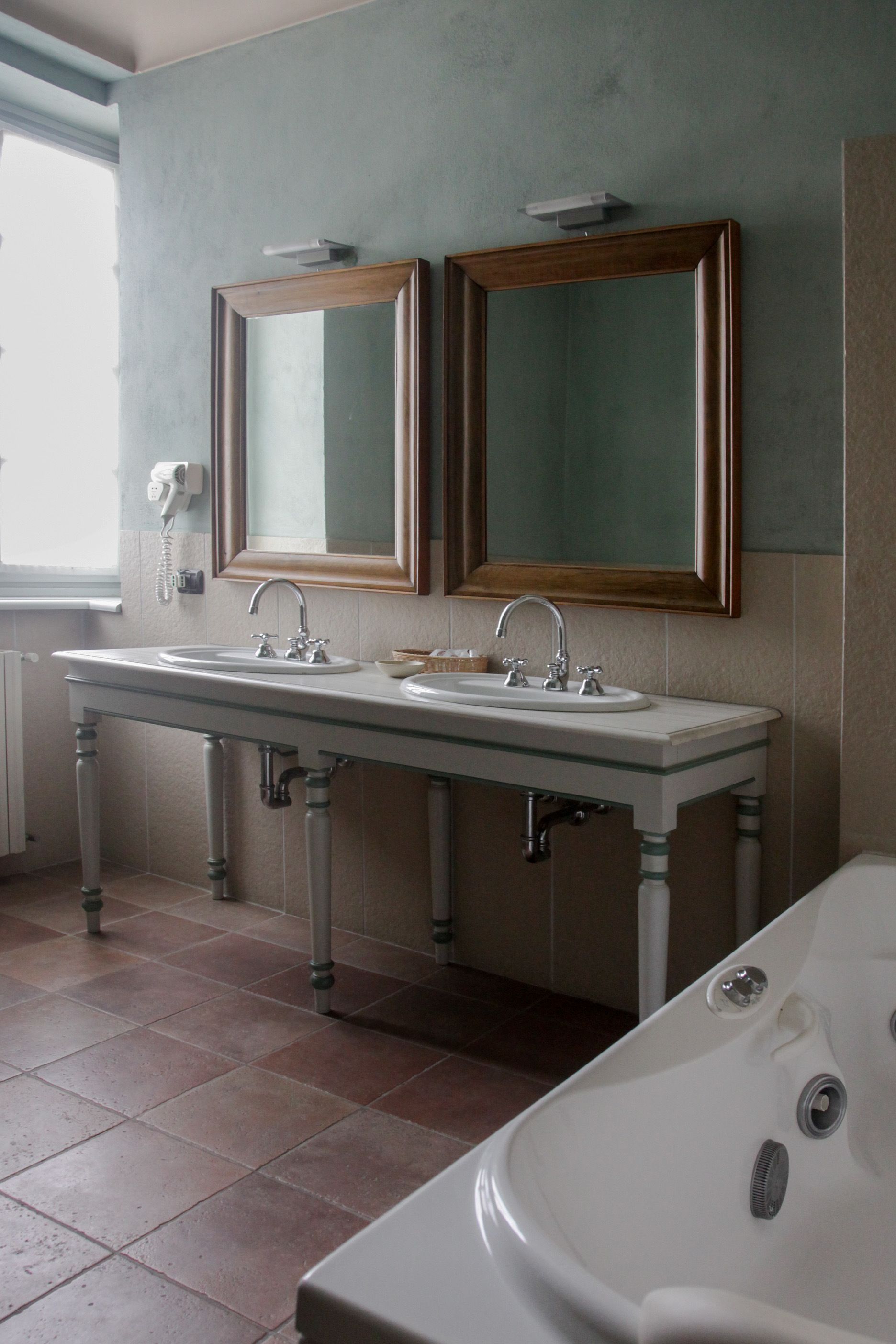 Une salle de bain avec un double vasque, deux miroirs, une baignoire et une fenêtre.