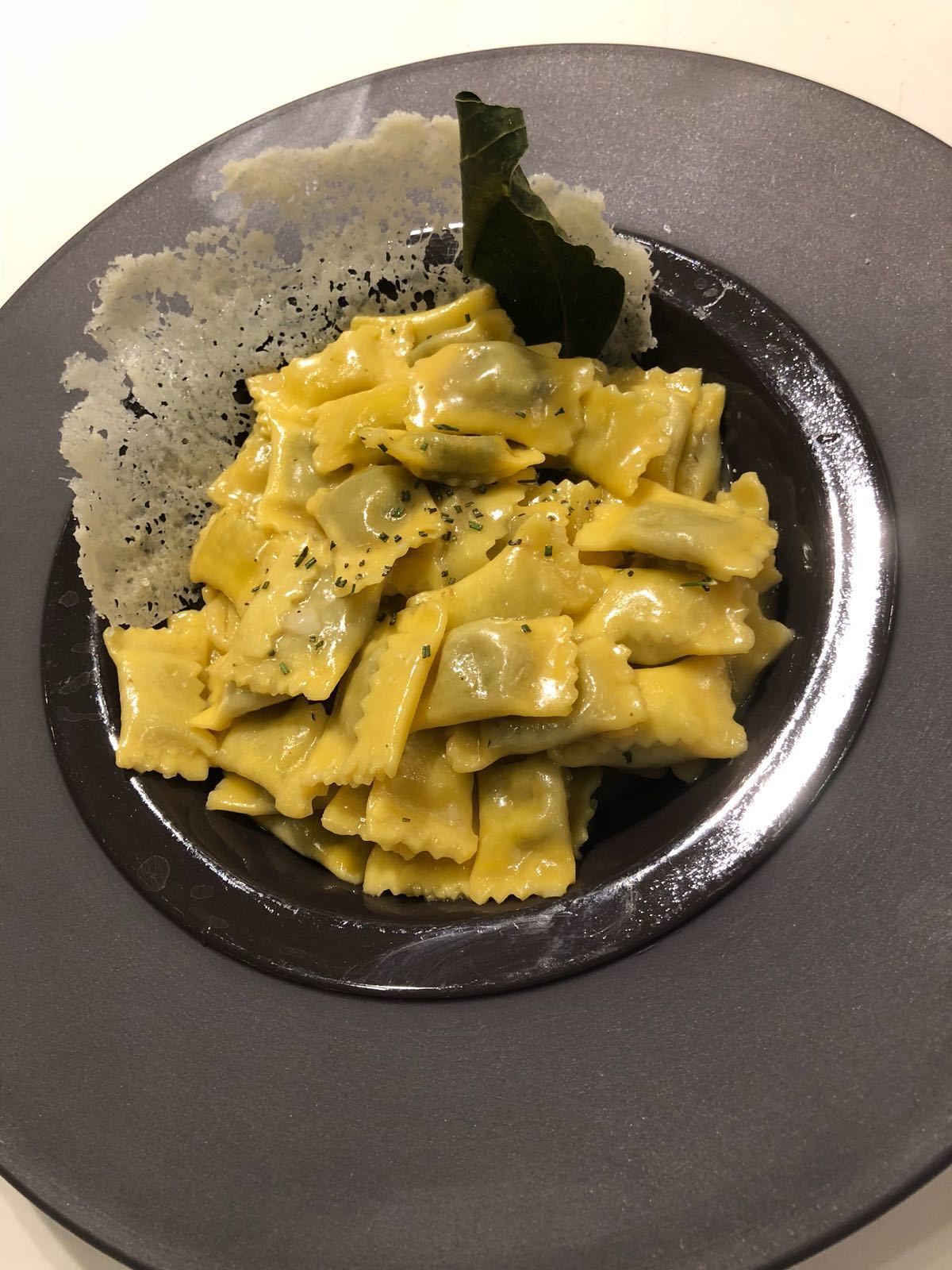 Un piatto di ravioli guarnito con erbe aromatiche e un foglio di alloro.