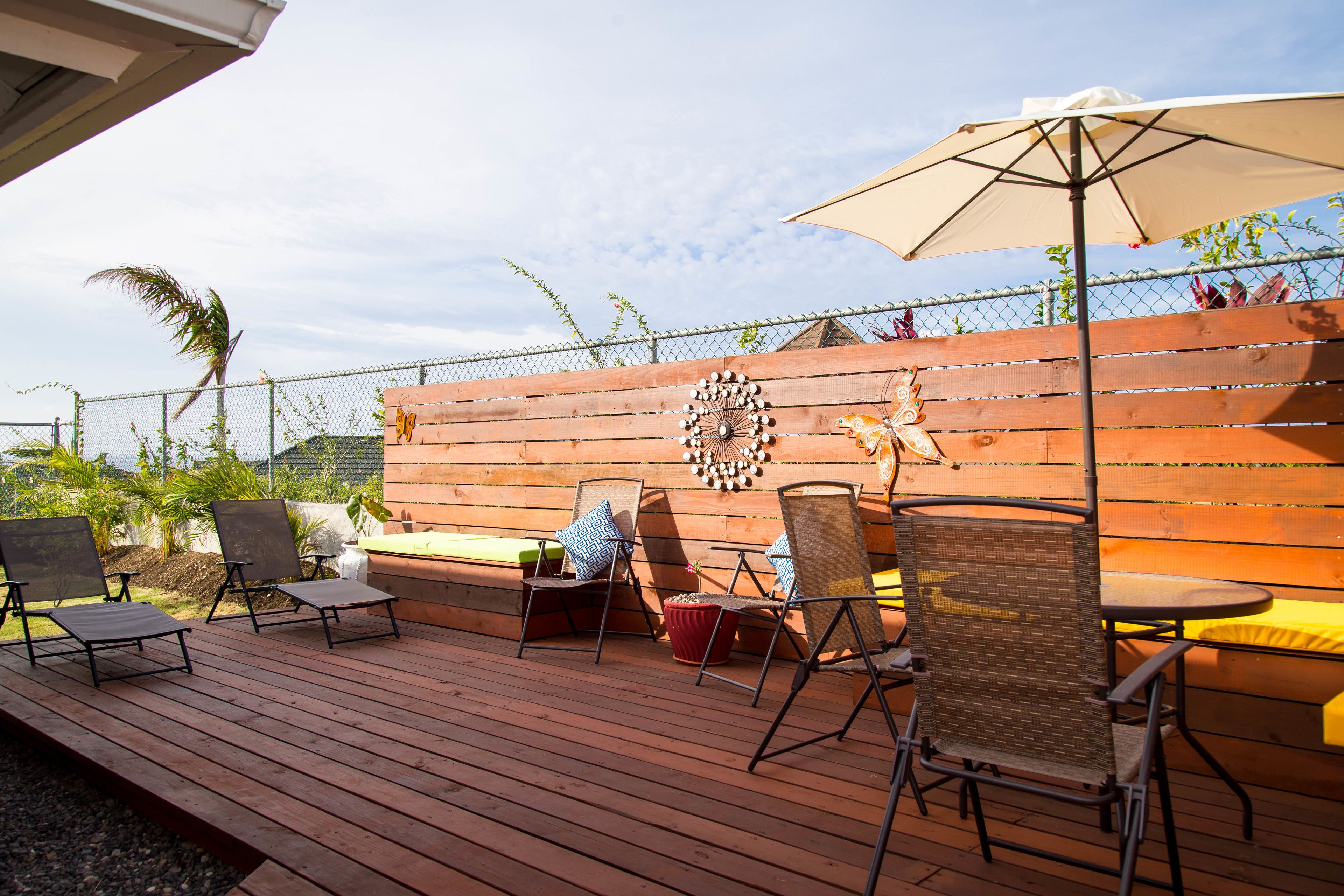 Une terrasse extérieure avec une plateforme en bois, des chaises en métal, une table et un grand parasol.