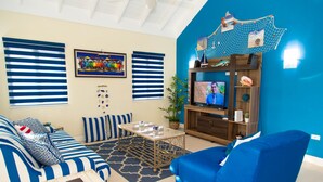 A living room with a blue sofa, striped cushions, a coffee table, and a television. - Ocho Rios Villa Azul at Coolshade XIII (St. Ann's Bay)