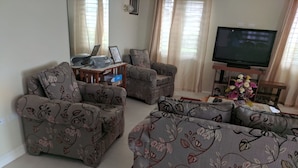 Ein Wohnzimmer mit floral geprägten Sofas, einem Fernseher und einem kleinen Tisch mit Dekorationsgegenständen.