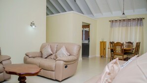 Uma sala de estar com sofá bege, mesa de centro de madeira e um espaço de jantar com mesa e cadeiras de madeira.