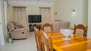 Uma sala de estar com sofá, poltrona reclinável, televisão e mesa de jantar com cadeiras.