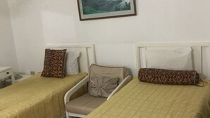 A hotel room with two beds, a chair, a small table, and a painting on the wall.