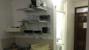 A compact kitchen with a stove, sink, and white cabinets. There are shelves above the counter holding various kitchen items.