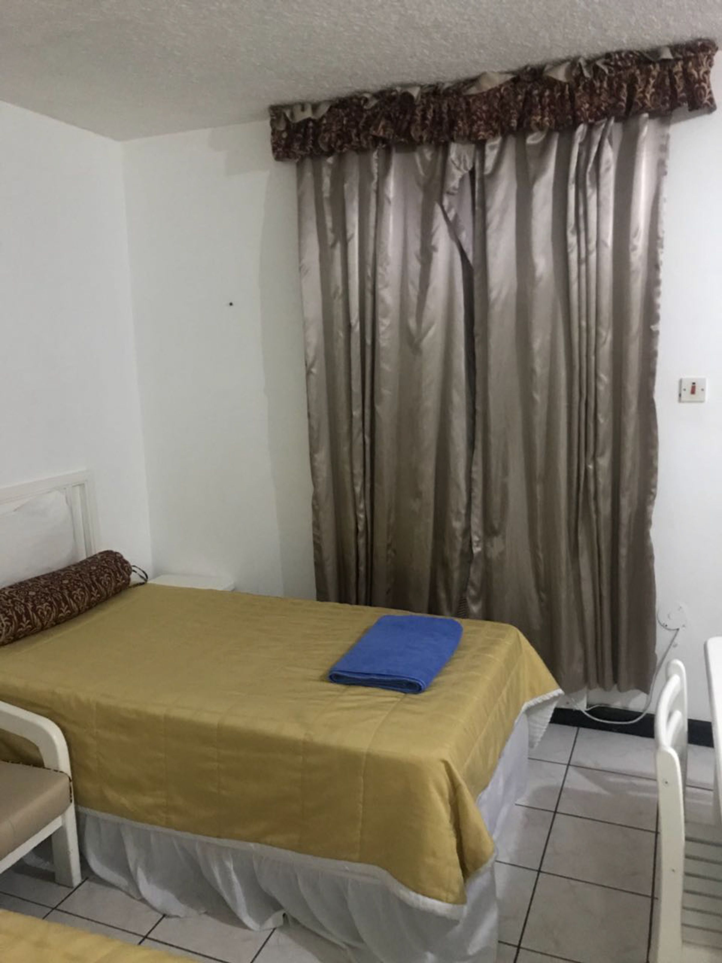 A small, clean room with a bed, a chair, and a curtain.