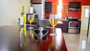 A kitchen with a red wall, a dining table with wine glasses and a bottle, and a pair of sunglasses on the table. - Ocho Rios TaylorMade Vacation Villas (Ocho Rios)