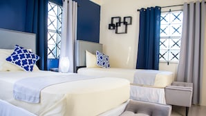 A hotel room with two beds, a grey upholstered bench, and a small table. - Ocho Rios TaylorMade Vacation Villas (Ocho Rios)