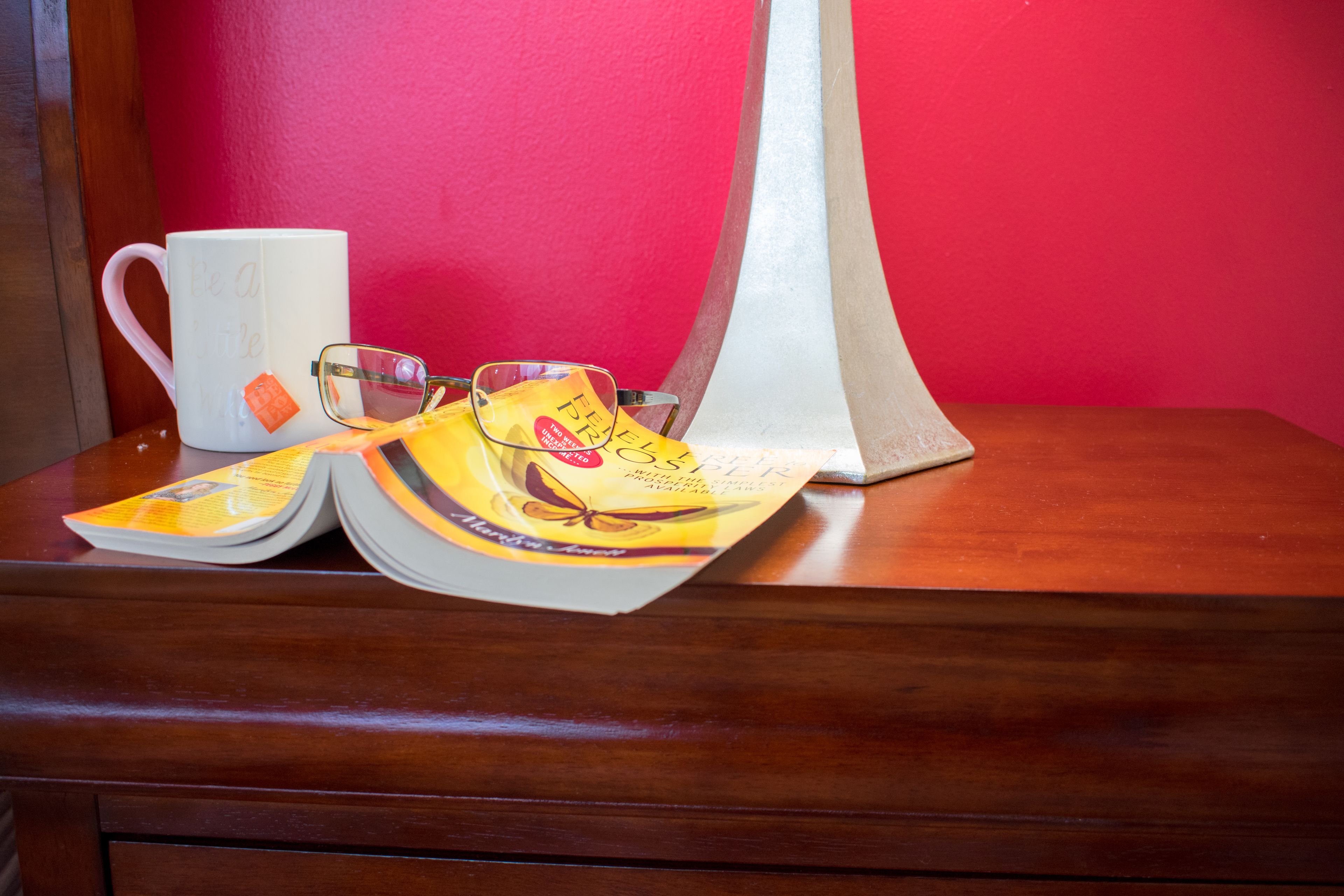 A wooden table with a white mug, a pair of glasses, and a book with a yellow cover.