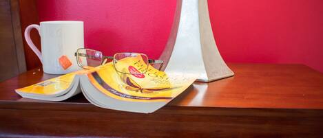 A wooden table with a white mug, a pair of glasses, and a book with a yellow cover.