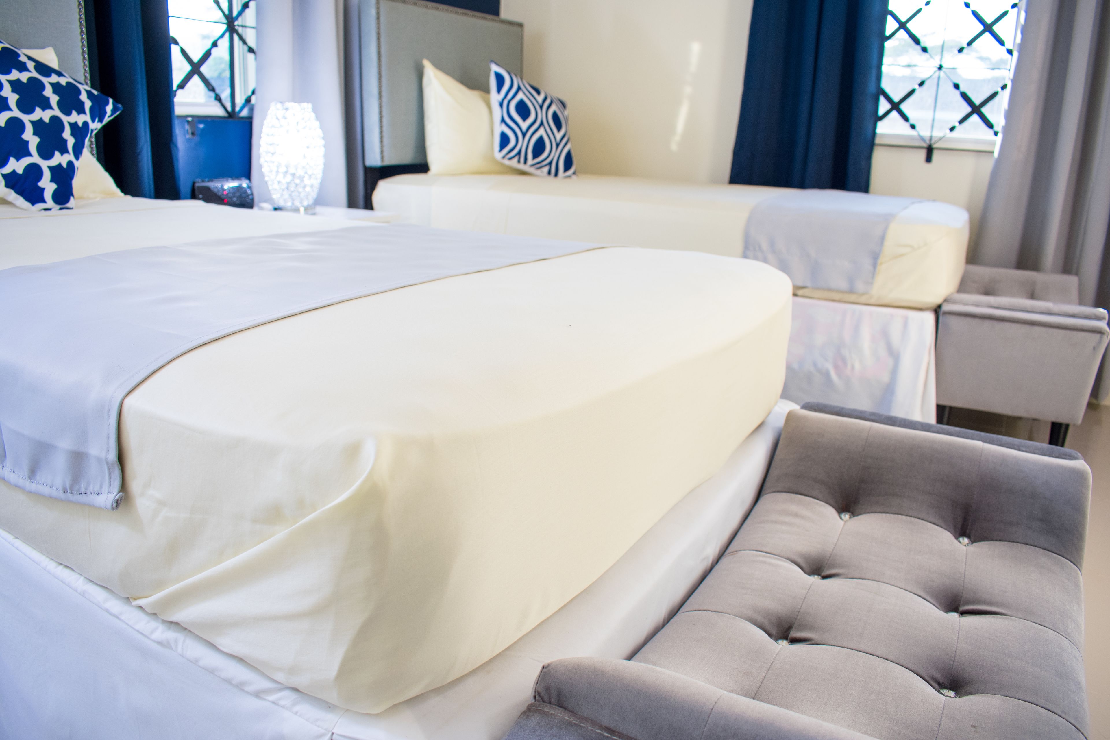 A hotel room with two beds, a grey upholstered armchair, and a bedside table.