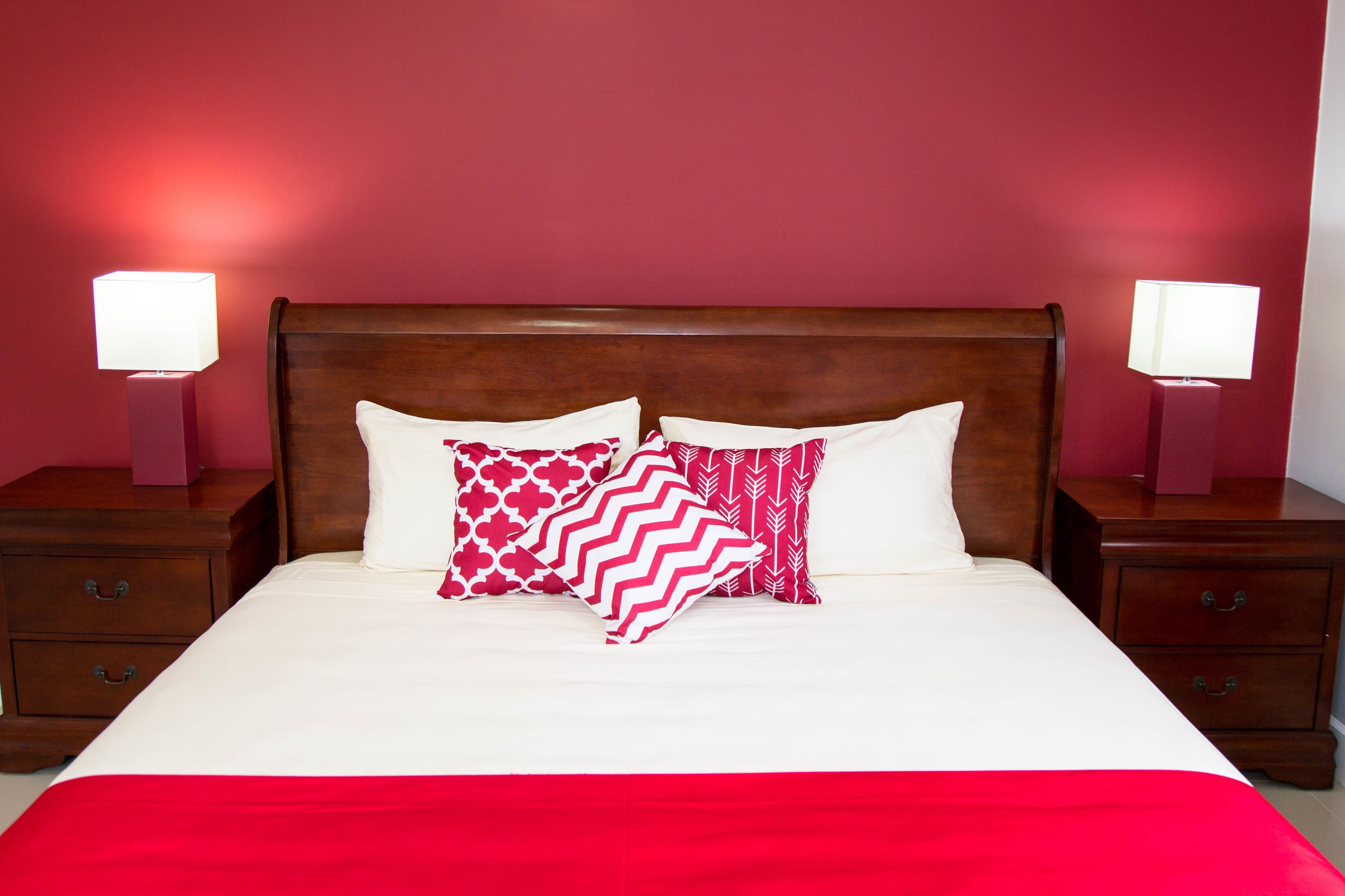 A neatly made bed with a red bedspread, two bedside tables with lamps, and a wooden headboard.