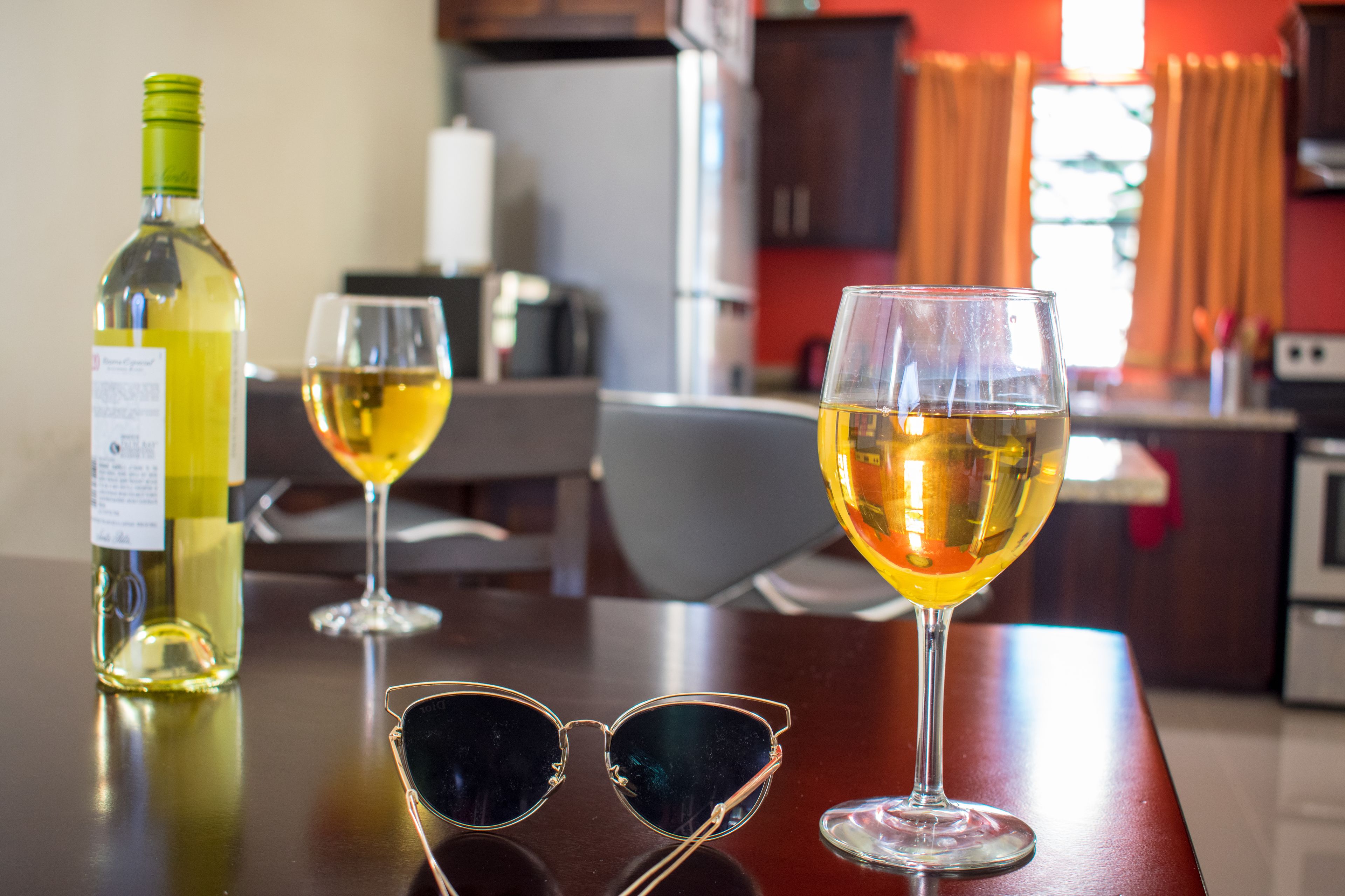 A table with a bottle of white wine, two wine glasses, and a pair of sunglasses.
