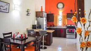 A modern kitchen with a red accent wall, stainless steel appliances, and a dining area with a wooden table and chairs. - Ocho Rios TaylorMade Vacation Villas (Ocho Rios)