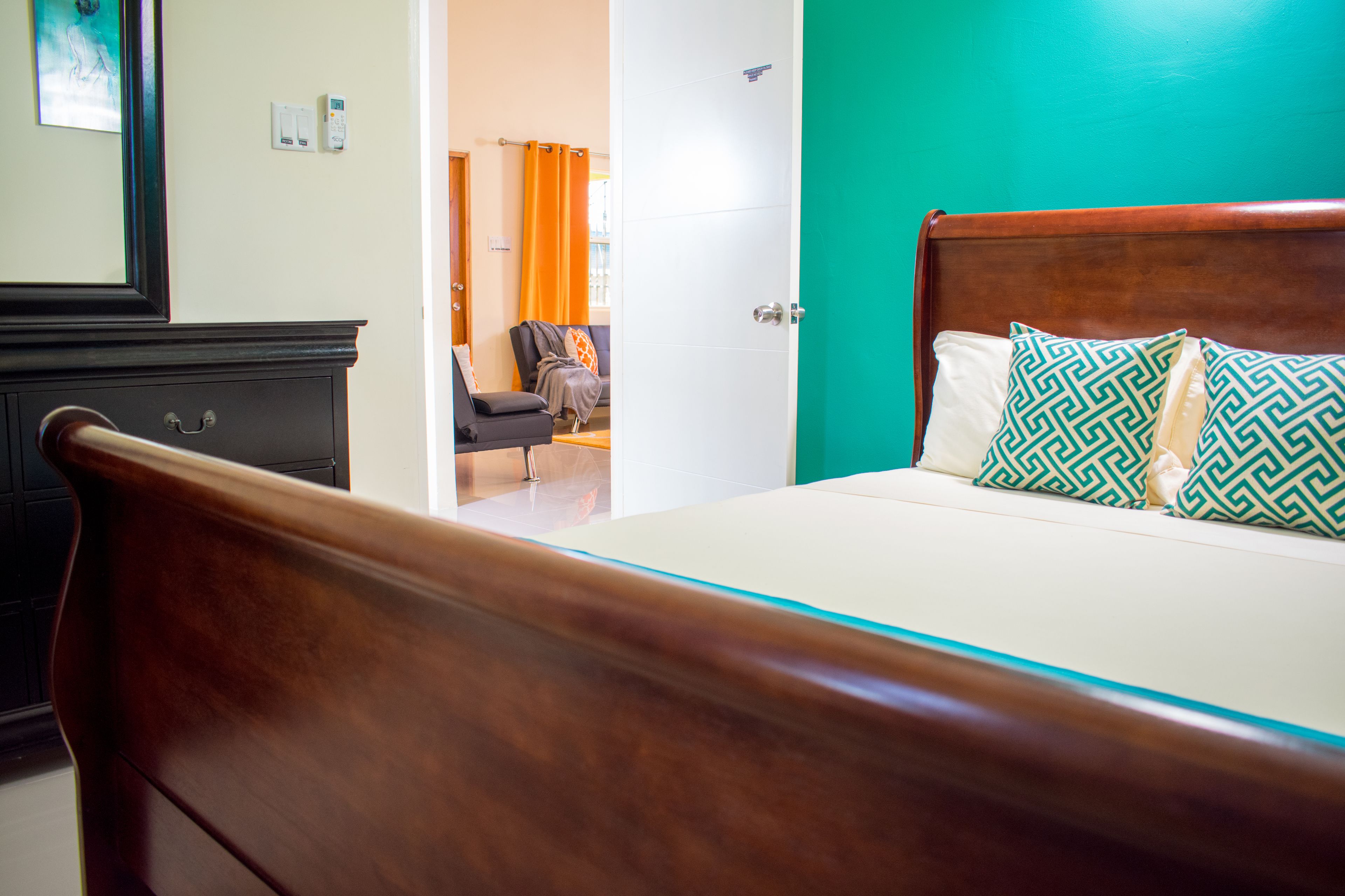 A hotel room with a wooden bed, a bathroom with a mirror, and a view of the hallway.