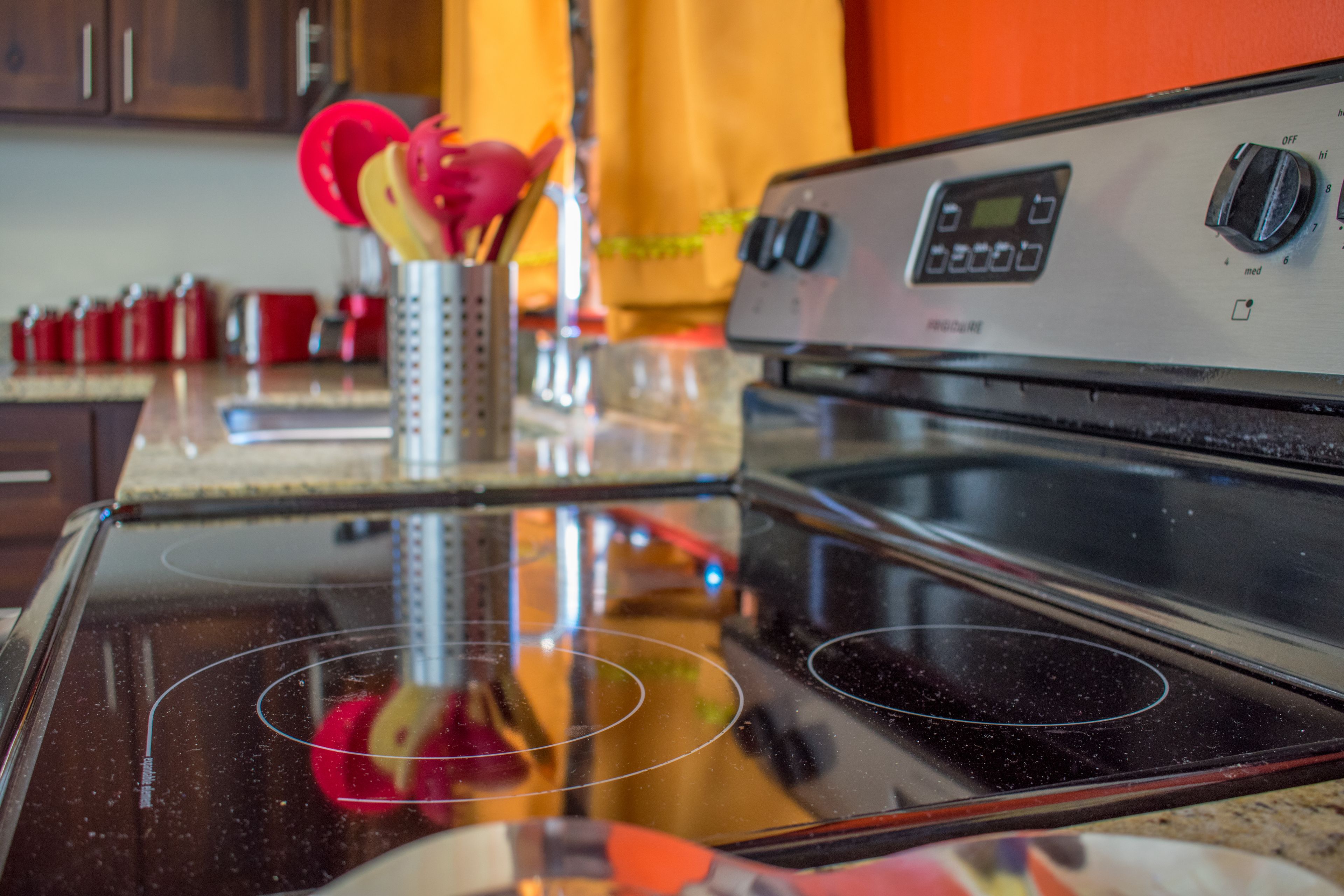 A kitchen with a stainless steel stove, a digital control panel, and a red utensil holder.