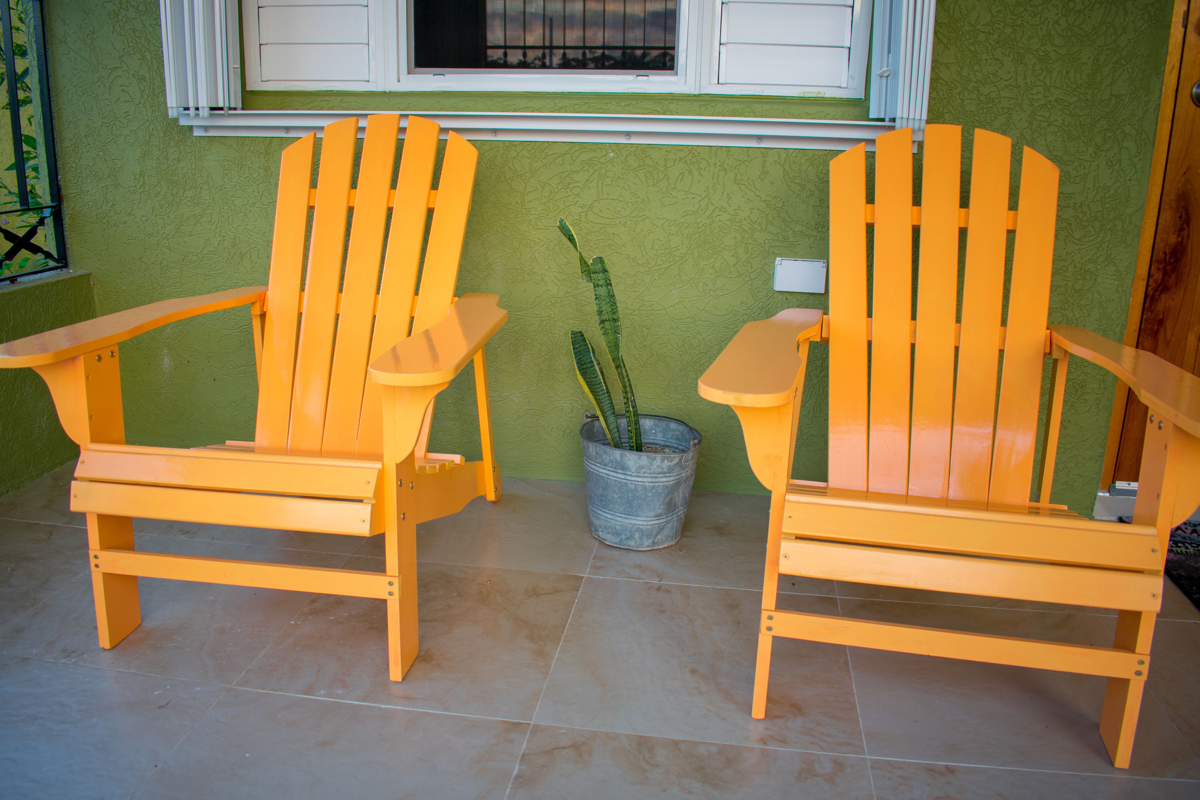 Two wooden Adirondack chairs with a potted plant between them.