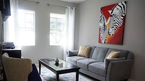 A living room with a grey sofa, a glass coffee table, a beige armchair, and a zebra painting on the wall. - New Kingston Guest Apt Surbiton (Kingston)