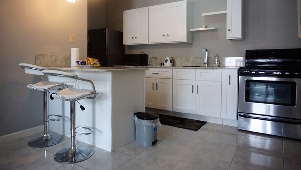 A modern kitchen with white cabinets, a stainless steel oven, and two bar stools. - New Kingston Guest Apt Surbiton (Kingston)
