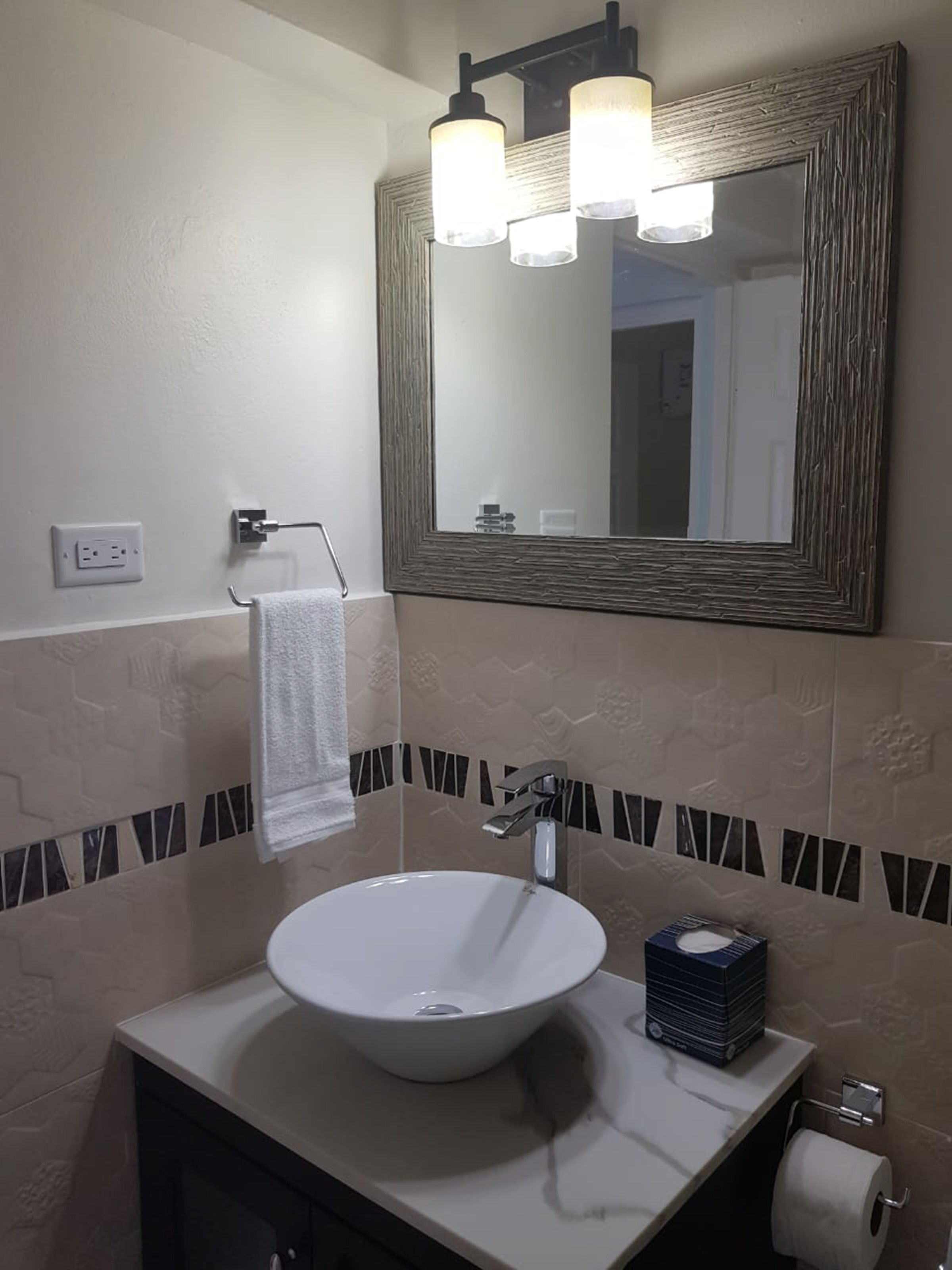 Une salle de bain avec un lavabo blanc, un miroir doté d’un cadre texturé et une serviette suspendue à un porte-serviettes.