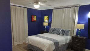 Quarto com cama, duas mesas de cabeceira, ventoinha no teto e duas luminárias na parede.