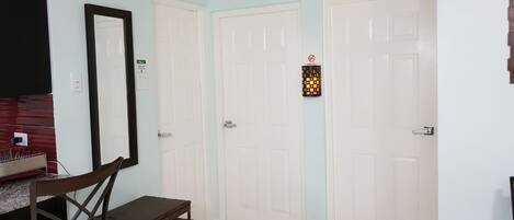A room with two white doors, a small table with chairs, a mirror, and a light fixture on one of the doors.