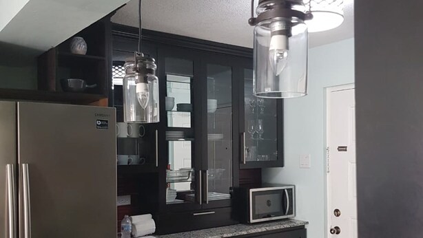 Uma cozinha moderna com armários escuros, geladeira de aço inoxidável, micro-ondas e bancada de granito.