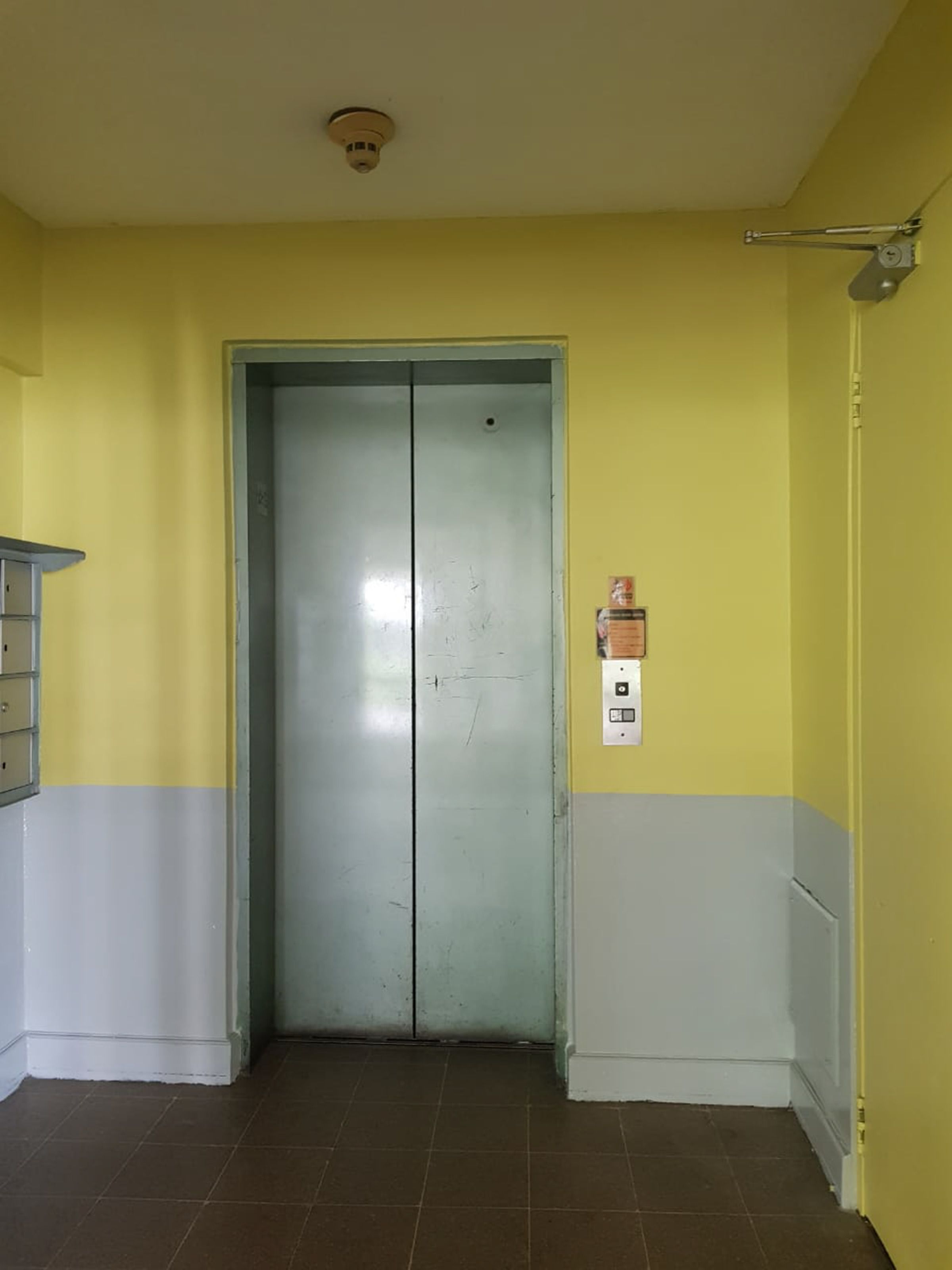 A closed elevator in a room with yellow walls and a white baseboard.