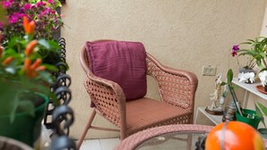 Una silla de mimbre con un cojín morado, una mesa de vidrio con una esfera naranja y plantas en macetas.