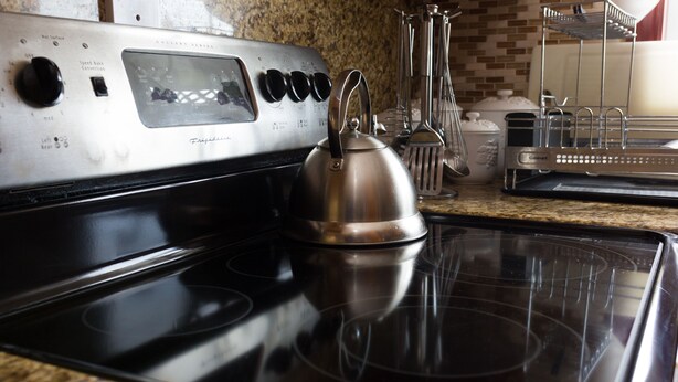 Una cocina con estufa de acero inoxidable, tetera y diferentes utensilios de cocina.