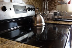 Una cocina con estufa de acero inoxidable, tetera y diferentes utensilios de cocina.
