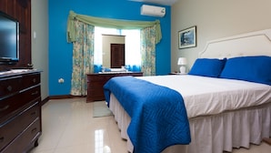 A bedroom with a large bed, a dresser, a mirror, and an air conditioning unit.