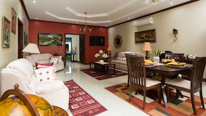 A spacious living room with a dining area, featuring a chandelier, sofas, and a dining table set with yellow napkins.
