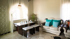 A living room with a sofa, a table, and a bench. There is a window with curtains, a plant, and a door with a geometric design. - Apartment in Hellshire near Beach (Hellshire)